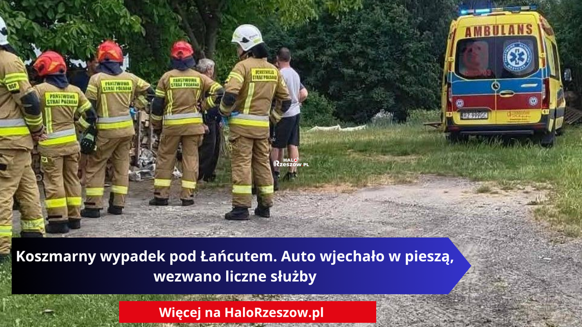 Koszmarny wypadek pod Łańcutem. Samochód wgniótł kobietę w ścianę budynku Miejsce wypadku drogowego w Husowie pod Łańcutem. Po lewej stronie stoi grupa strażaków w mundurach bojowych Państwowej Straży Pożarnej i OSP. Po prawej stronie na trawiastym poboczu zaparkowana jest żółta karetka pogotowia ratunkowego z włączonymi sygnałami świetlnymi i napisem Ambulans.