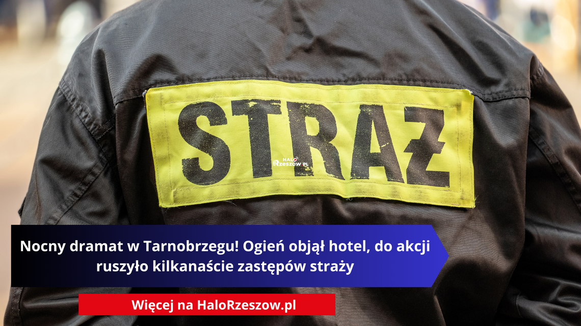 Plecy strażaka w czarnym mundurze z żółtą naszywką STRAŻ oraz nałożonym napisem informującym o nocnym pożarze hotelu w Tarnobrzegu.