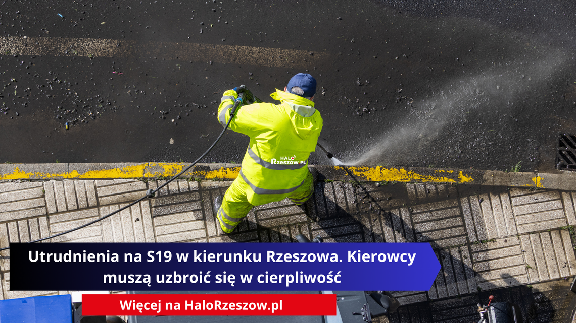 Pracownik w żółtym stroju ostrzegawczym myje nawierzchnię drogową myjką ciśnieniową.